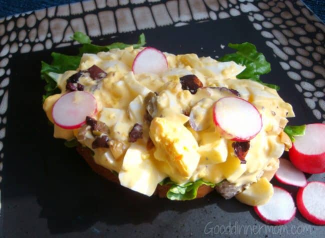  open faced Egg Salad with radishes and black olives served on a black plate
