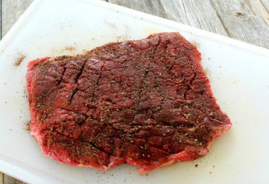 seasoned flank steak on a white cutting board