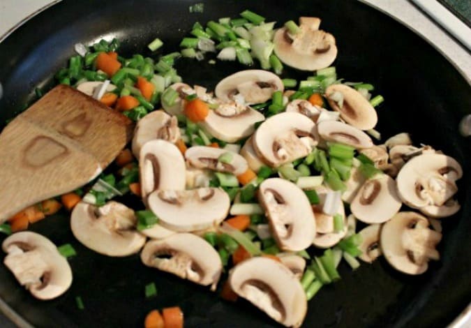  mushrooms, onions and carrots in a black pan with wooden spoon