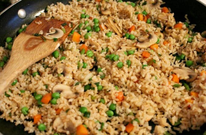 Rice, peas, carrots, shallots cooking in a pan with a wooden spoon