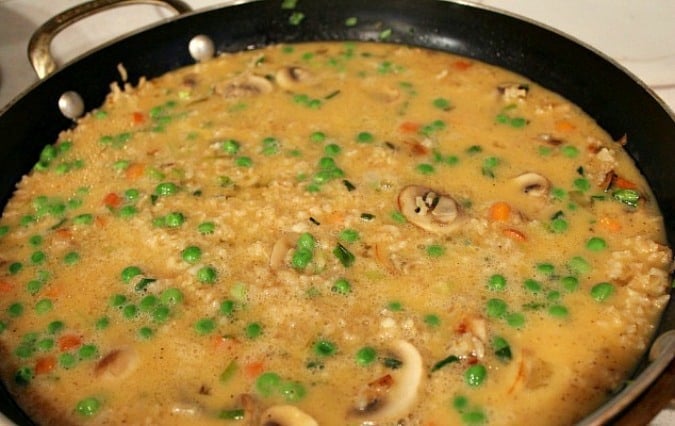 Rice, egg, mushrooms, peas, carrots and onions cooking in a pan
