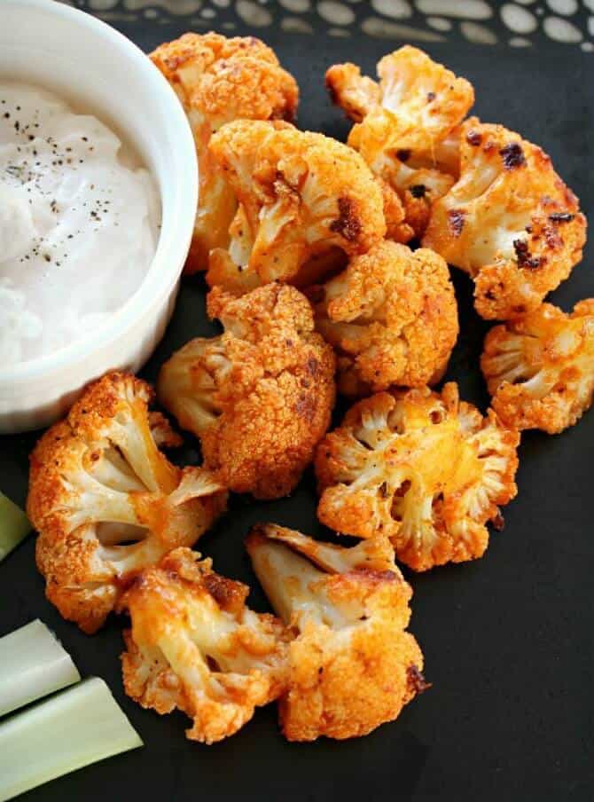 Buffalo cauliflower bites with dipping sauce on the side served on a black plate