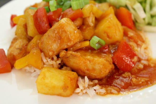  Sweet and Sour Chicken with pineapple, peppers and green onions served over rice on a white plate 