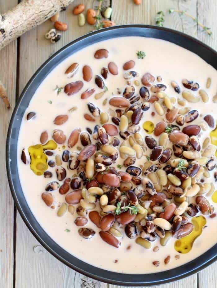 Heirloom beans in cream in black bowl with olive oil on top