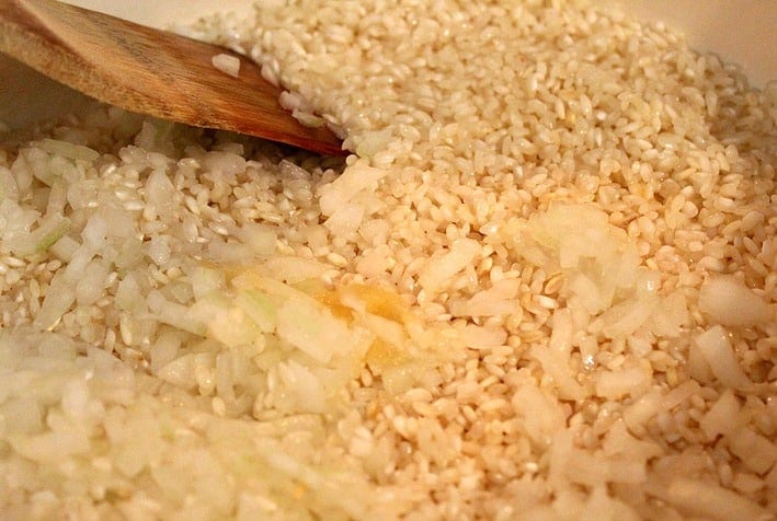 Risotto being cooking in a pan, stirred with a wooden spoon