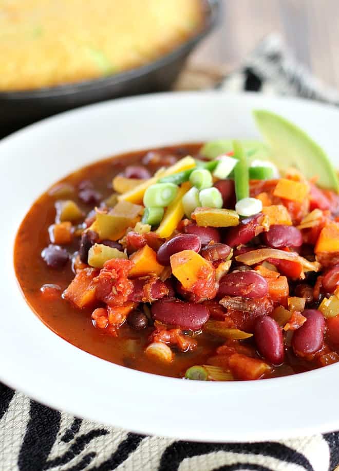 Hearty Vegan chili with fresh vegetables topped with green onions served in a white bowl