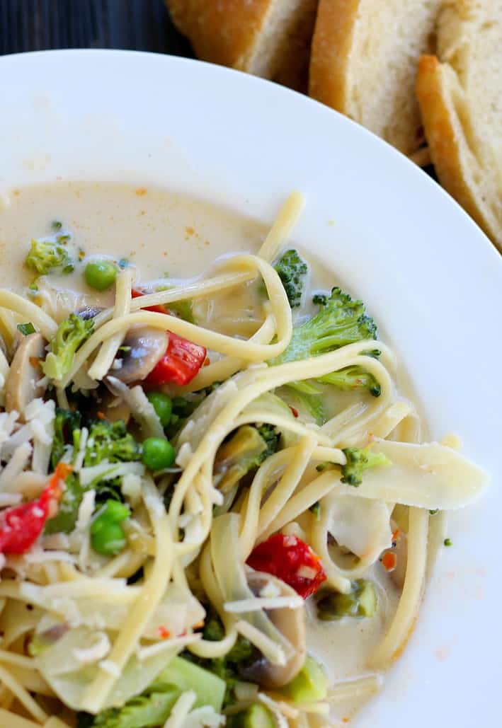 Close up of Pasta Primavera served on a white plate with bread on the side