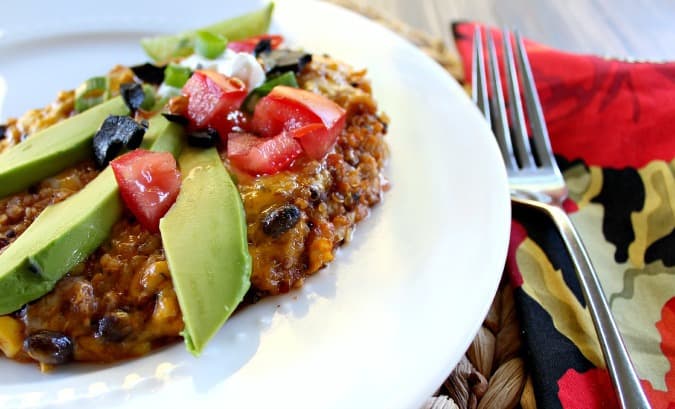 Quinoa Black Bean Enchilada Casserole topped with avocados, olive and tomatoes on a white plate