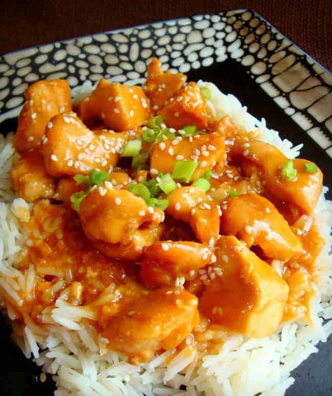 Sesame Chicken over rice served on a black and white plate