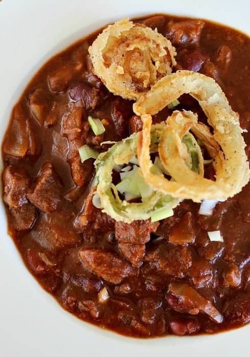 Amazing Slow Cooker Texas Chili in a white bowl topped with onions and onion rings