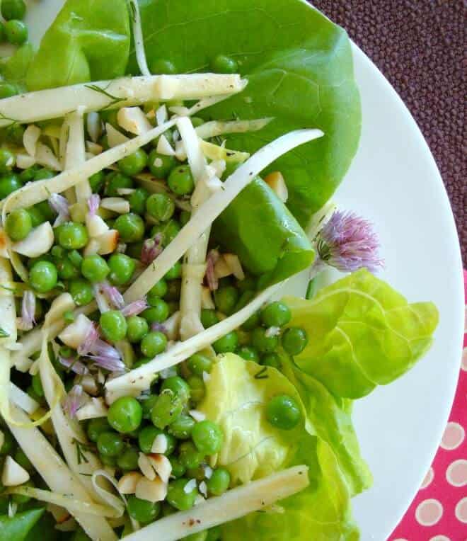 Butter Lettuce Spring Salad topped with cheese and peas on a white plate