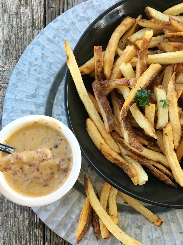 Aioli sauce with olives in a white bowl served with fries in a black bowl