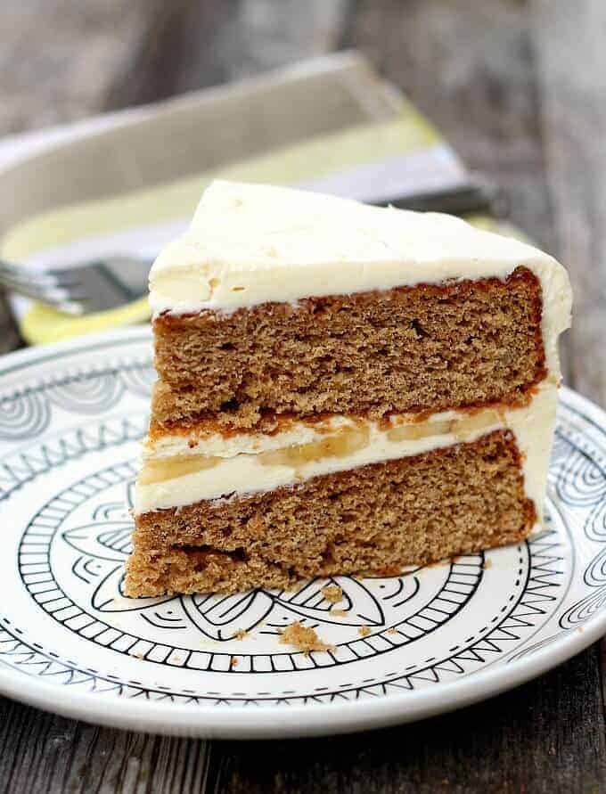 Slice of banana cake with cream cheese frosting on white plate