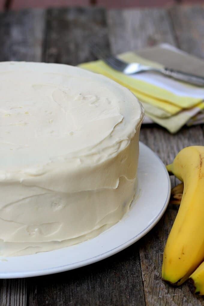 banana cake with cream cheese frosting before being cut. Banana and fork on napkin in background