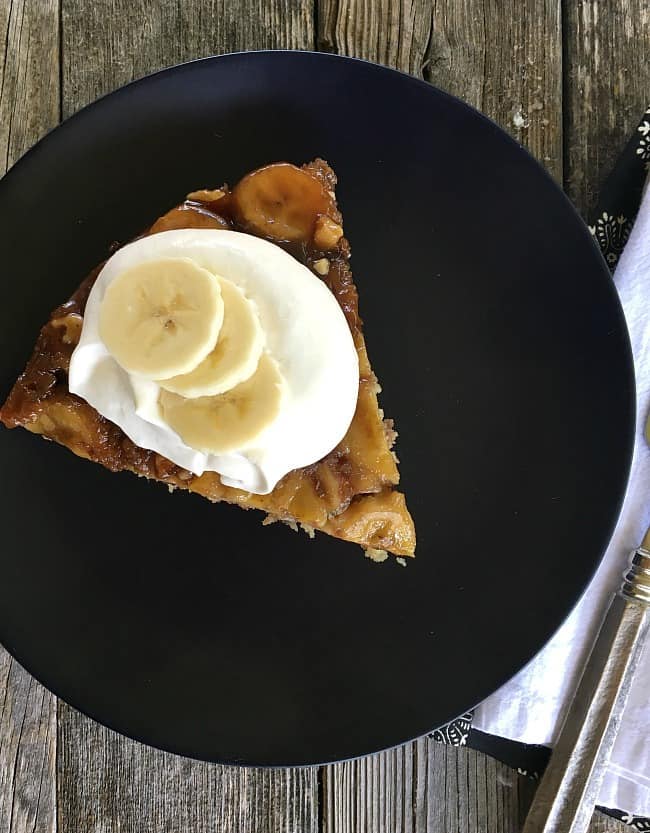 top view of a slice of banana upside down cake with whipped cream on black plate