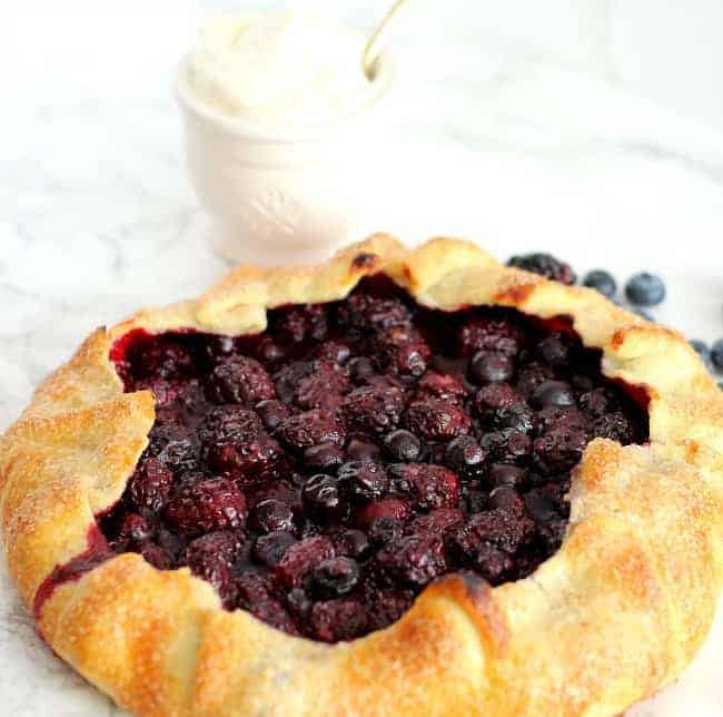 berry galette on marble surface with whipped cream in a cup