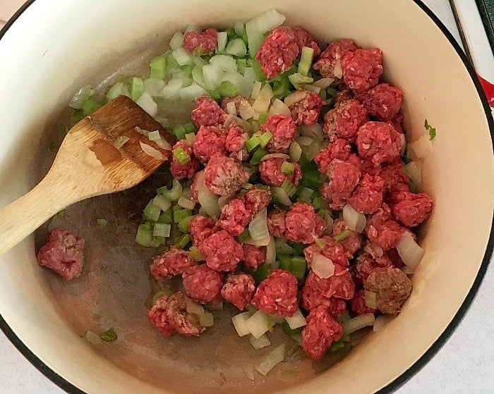 Onions, celery and beef in pot with wooden spoon