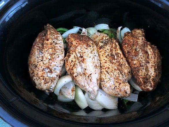 seasoned chicken on top of chopped onions and peppers in slow cooker