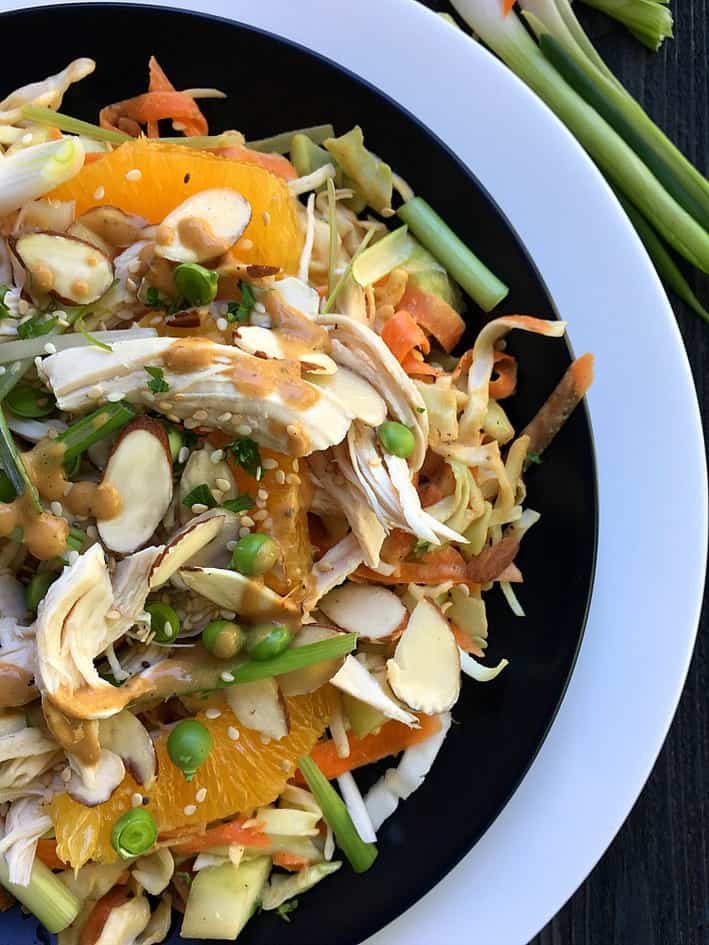  Chinese Chicken Salad in a black and white bowl with chicken, oranges, almonds, sesame seeds and peanut dressing.
