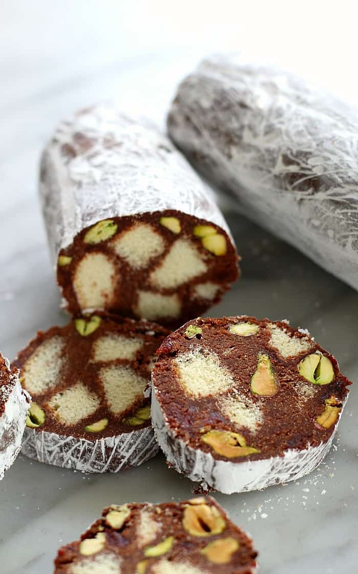chocolate salami cookies, partly sliced. Powdered sugar covers loaf, cookies have pieces of cookie and pistachios