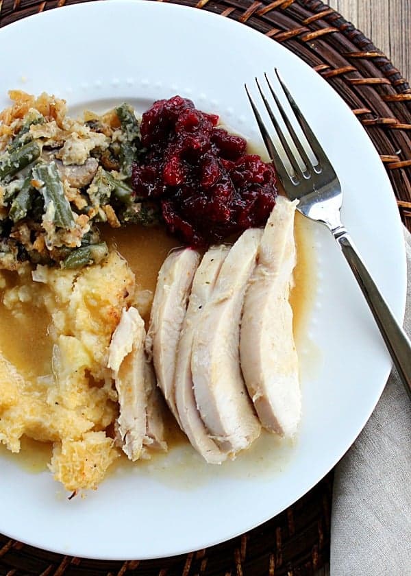 sliced turkey on a white plate with cranberry sauce, green bean casserole, mashed potatoes