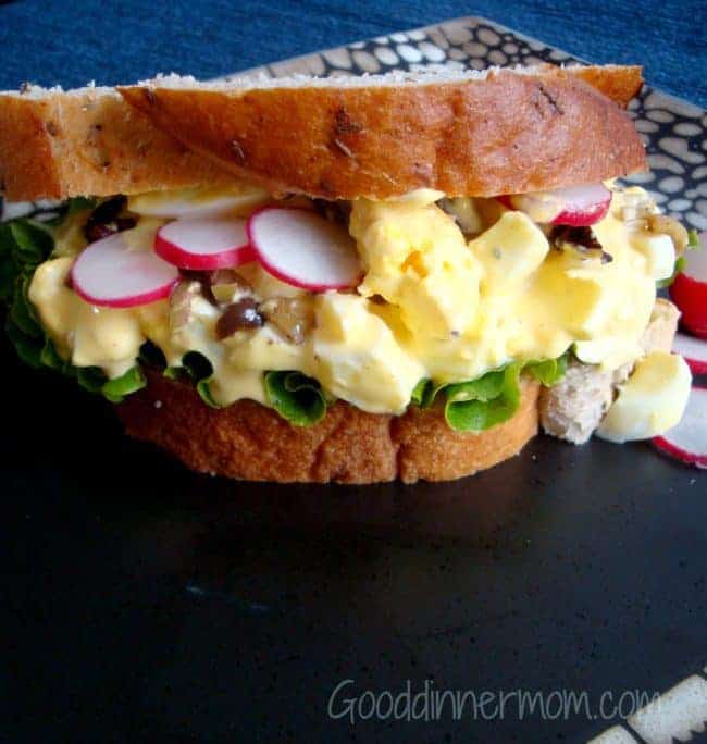 Company Worthy Egg Salad on two slices of bead with radishes and lettuce served on a black plate