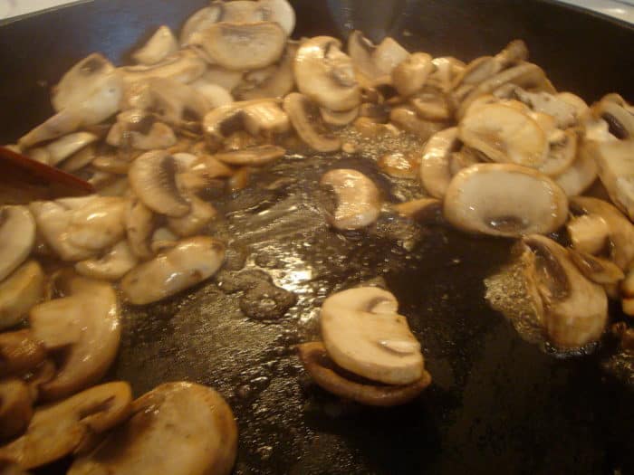 sliced mushrooms cooking in a black skillet
