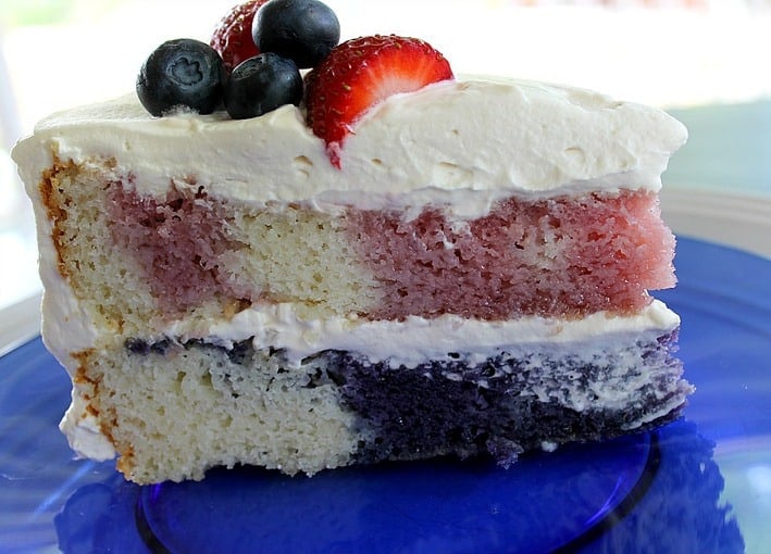 One slice of Poke Cake with whipped cream frosting and berries on a blue plate