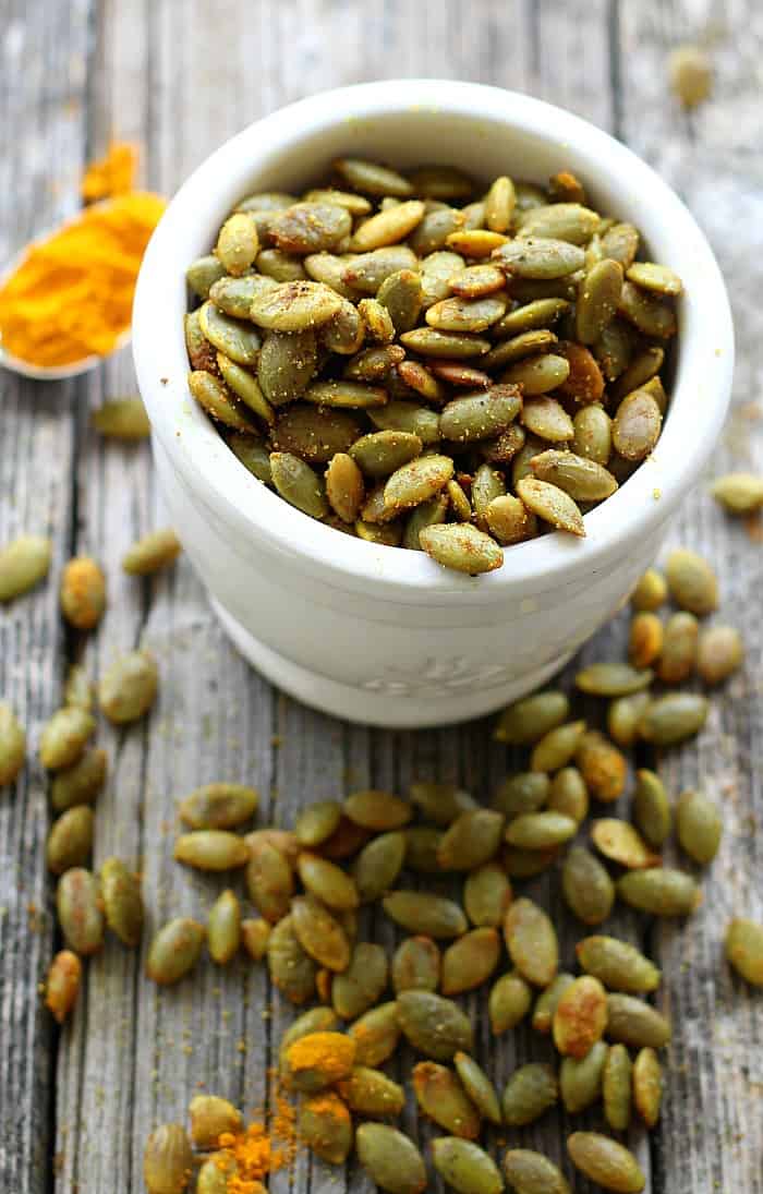 Turmeric Roasted Pumpkin Seeds in a white bowl with seeds and turmeric on the table 